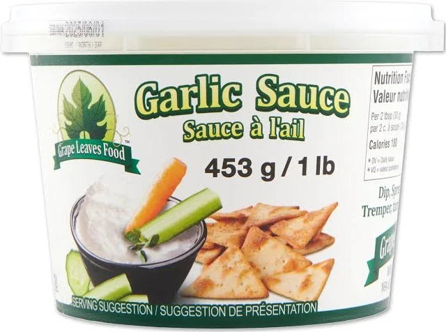 A jar of Grape Leaves Garlic Sauce with fresh garlic and grape leaves in the background, showcasing the flavorful Mediterranean condiment.