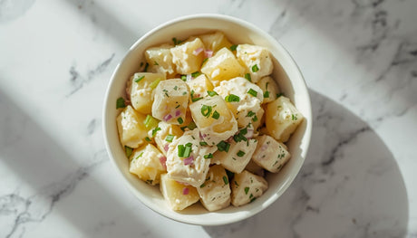 Fresh potato salad recipe with cubed potatoes coated in creamy dressing in a white bowl
