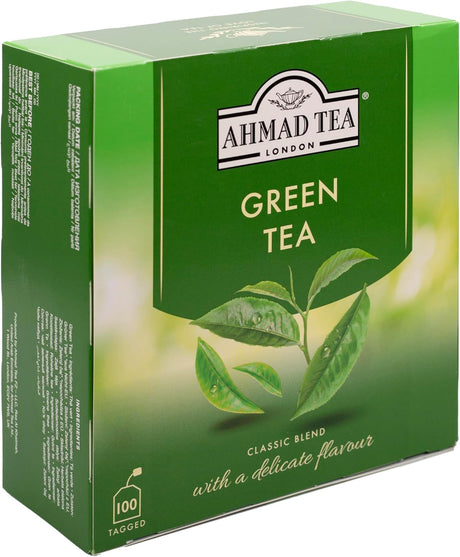 A box of Ahmad Tea Green Tea with green tea leaves and packaging, showcasing the brand and fresh, natural tea leaves inside.